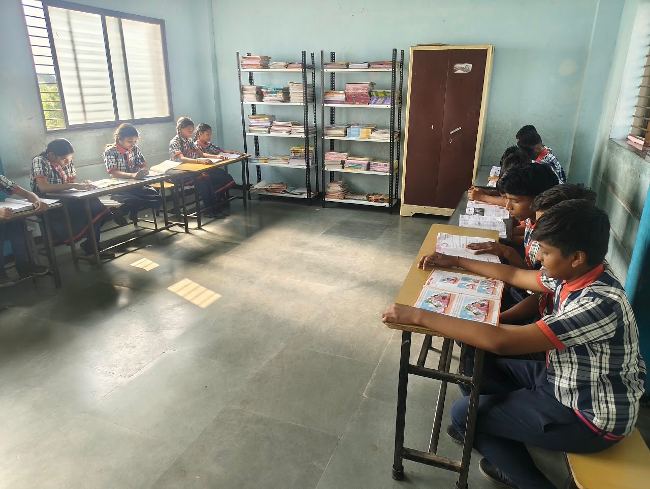 Pupils reading at desks beside shelves stacked with books in the reading room at Sunrise Convent School, Bhensola